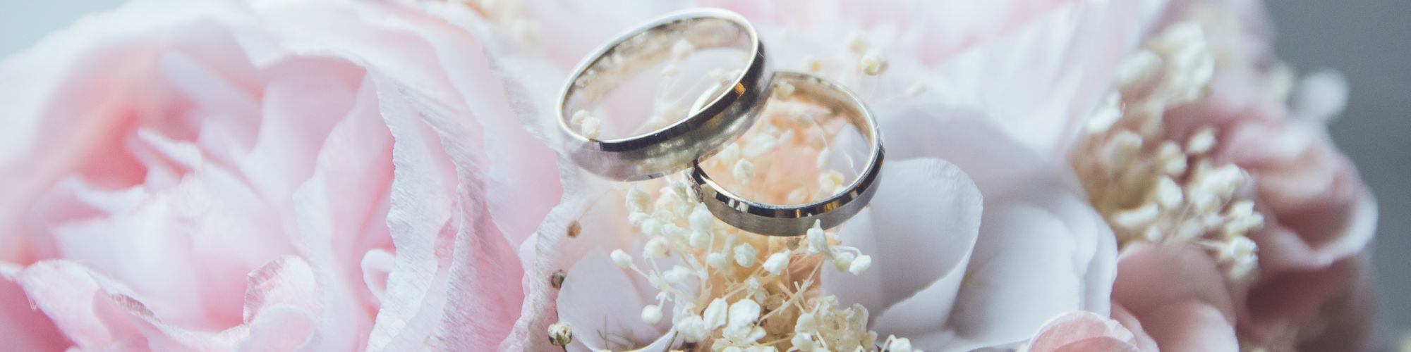 A pair of wedding rings placed on a bouquet of pink roses and white baby's breath flowers, creating a romantic and elegant ambiance.