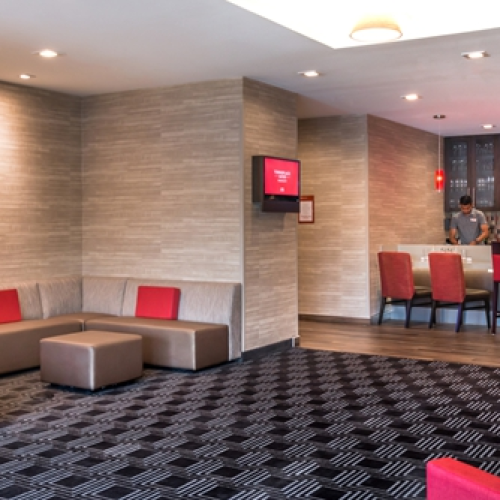 A modern lounge area with brown and red seating, a patterned carpet, and a bar with stools in the background, featuring contemporary lighting.