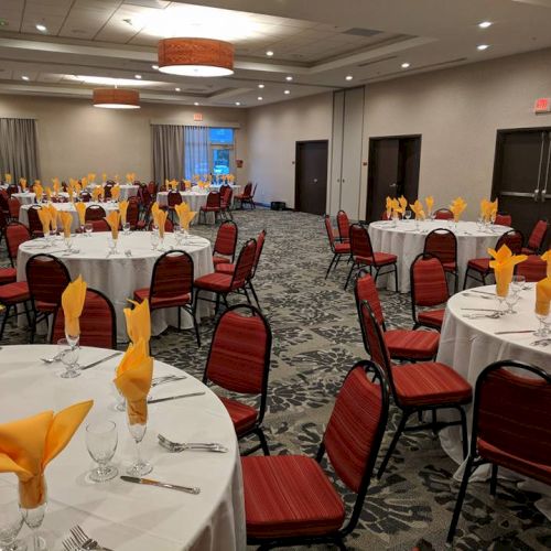 A banquet room with round tables set for an event, featuring yellow napkins, red chairs, and neatly arranged tableware.