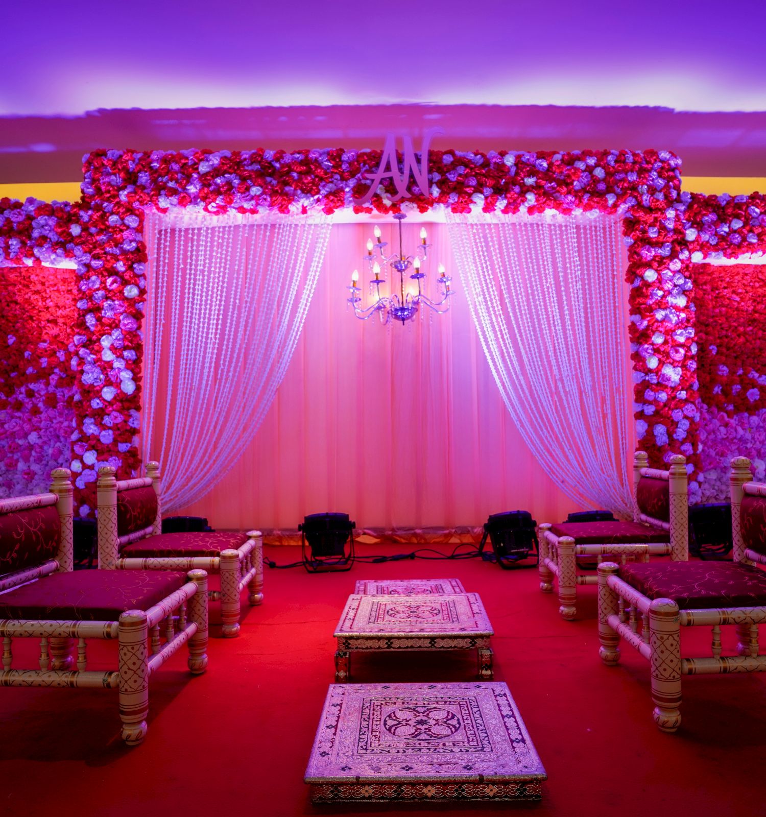 This image shows a vibrant, elegantly decorated stage setup with ornate seats, floral arrangements, and purple lighting, possibly for a wedding or event.