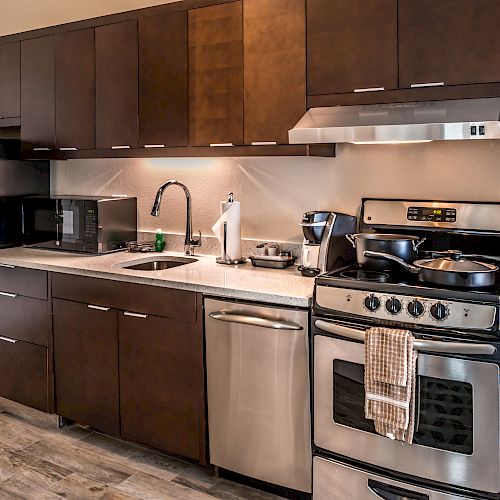 A modern kitchen with wooden cabinets, stainless steel appliances, a refrigerator, microwave, sink, stove, and dishwasher.